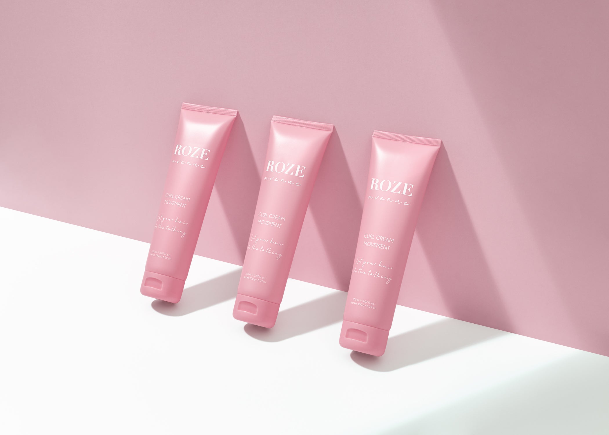 Trzy kremy do loków Roze Avenue oparte o ścianę