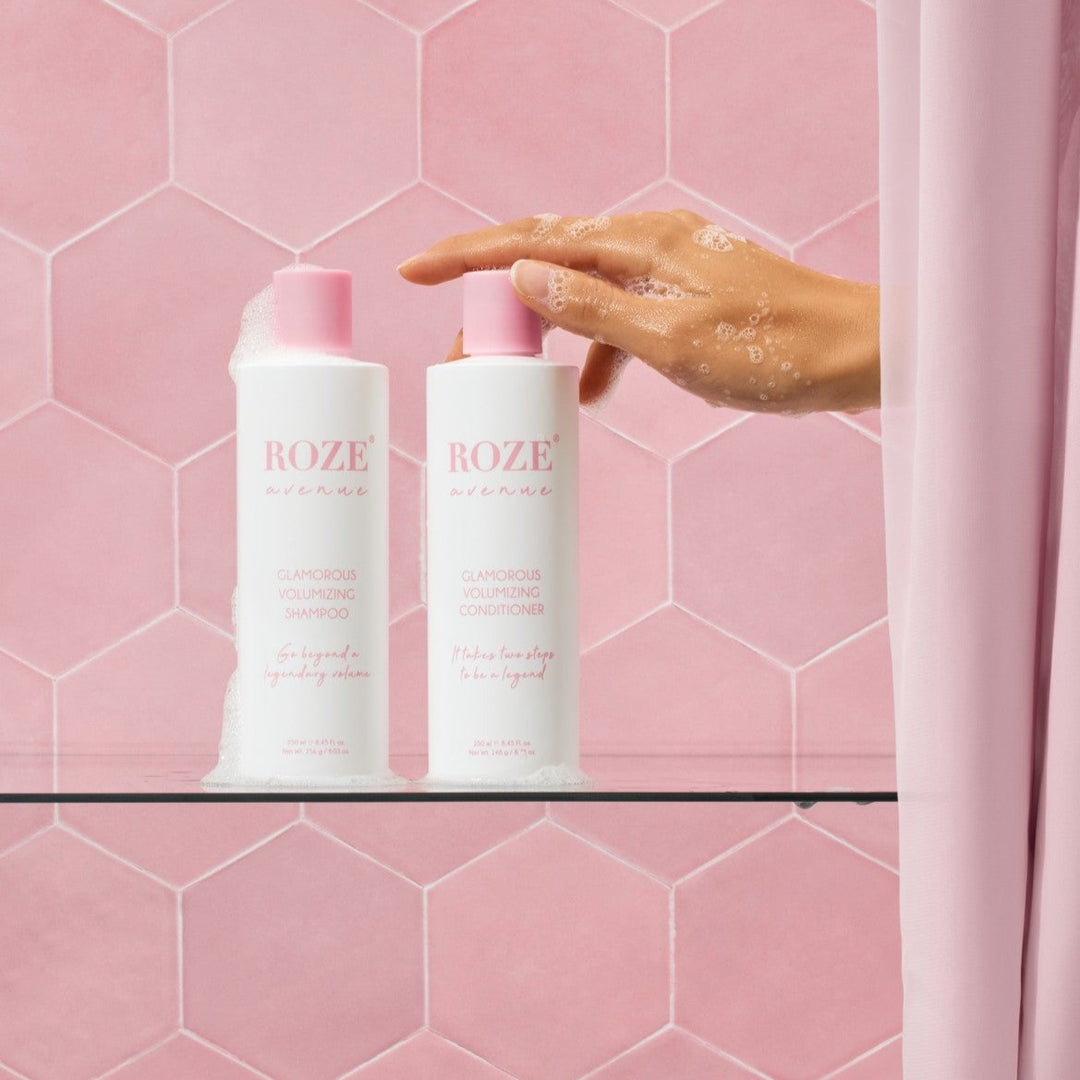 szampon i odżywyka Roze Avenue - glamorous volumizing shampoo i conditioner ustawione obok siebie na szklanej półce, ręka kobiety spod prysznica sięga po odżywkę