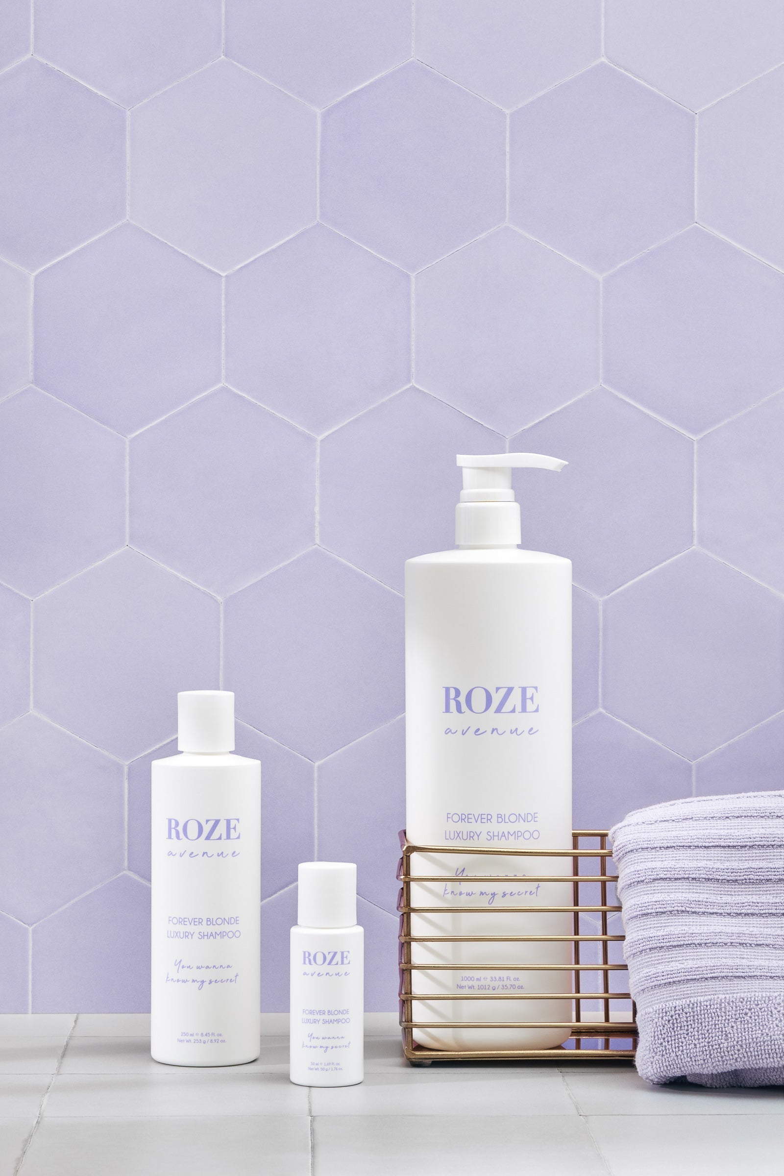 Trzy szampony do włosów blond roze avenue - Mini, średni i duży położony w koszyku z fioletowym ręcznikiem